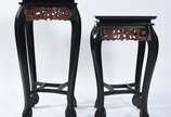 Duas colunas orientais de madeira pintada de pr... - Duas colunas orientais de madeira pintada de preto, saias com entalhes florais na cor rouge de fer, tampos quadrangulares sobre quatro pernas re...