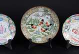 Três pratos de porcelana chinesa, sendo um par ... - Três pratos de porcelana chinesa, sendo um par com figura típica ao centro em policromia, e um prato decorado com figuras de galináceos e guirla...