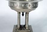 Fruteira com base de metal prateado decorado co... - Fruteira com base de metal prateado decorado com folhas de parreira e cachos de uvas em relevo, base quadrangular com quatro colunas sustentando...