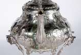 Samovar Art Nouveau de metal prateado ingles, c... - Samovar Art Nouveau de metal prateado ingles, contrastado, trabalhado com folhagens em relevo. Pega da tampa na forma de pássaro. Desgastes.