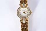 Bulova (1875),  - Relógio feminino de metal dourado e detalhes em  metal, mostrador branco com números e ponteiros dourados. Na caixa, funcionando.