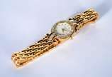 Bulova (1875),  - Relógio feminino de metal dourado e detalhes em  metal, mostrador branco com números e ponteiros dourados. Na caixa, funcionando.