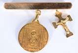 Alfinete de ouro 18 k., com pendentes represent... - Alfinete de ouro 18 k., com pendentes representando crucifixo com figura de Cristo e medalha sacra. (Por motivos de segurança a peça não se enco...