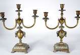 Par de candelabros de metal dourado para 3 vela... - Par de candelabros de metal dourado para 3 velas cada com base feitio ânfora com alças.