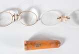 Três peças, sendo: dois pince nez e uma piteira... - Três peças, sendo: dois pince nez e uma piteira de âmbar com detalhes em ouro. No estojo. Um dos pince nez com arranhado e lascado.