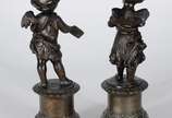 Par de antigas esculturas de petit bronze, repr... - Par de antigas esculturas de petit bronze, representando casal de crianças anjos, sobre pedestais com flores em relevo. Desgastes no metal.