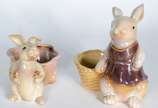 Duas esculturas de porcelana policromada repres... - Duas esculturas de porcelana policromada representando coelhos com cestos.