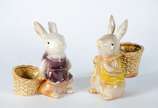 Duas esculturas de porcelana policromada repres... - Duas esculturas de porcelana policromada representando coelhos com cestos.