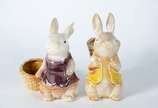 Duas esculturas de porcelana policromada repres... - Duas esculturas de porcelana policromada representando coelhos com cestos.