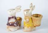 Duas esculturas de porcelana policromada repres... - Duas esculturas de porcelana policromada representando coelhos com cestos.
