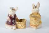 Duas esculturas de porcelana policromada repres... - Duas esculturas de porcelana policromada representando coelhos com cestos.