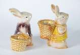 Duas esculturas de porcelana policromada repres... - Duas esculturas de porcelana policromada representando coelhos com cestos.