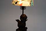 Luminária de petit bronze, base com figura de a... - Luminária de petit bronze, base com figura de anjo com pequena pomba nas mãos,  manga de vidro mesclado em diversos tons.