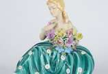 Estatueta de porcelana policromada representand... - Estatueta de porcelana policromada representando jovem com flores. Pétalas com lascados.