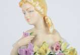 Estatueta de porcelana policromada representand... - Estatueta de porcelana policromada representando jovem com flores. Pétalas com lascados.