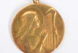Medalha de ouro 18 k., decorada com figura de m... - Medalha de ouro 18 k., decorada com figura de menina com harpa.  (Por motivos de segurança a peça não se encontra na loja).
