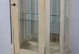 Vitrine de madeira patinada, parte inferior com... - Vitrine de madeira patinada, parte inferior com uma porta almofadada encimada por porta frontal e laterais de vidro, prateleiras internas também...