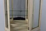 Vitrine de madeira patinada, parte inferior com... - Vitrine de madeira patinada, parte inferior com uma porta almofadada encimada por porta frontal e laterais de vidro, prateleiras internas também...