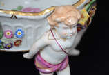 Fruteira de porcelana alemã Schierholz , sendo ... - Fruteira de porcelana alemã Schierholz , sendo prato central sustentando por quatro figuras angelicais em policromia, uma delas com restauro, al...