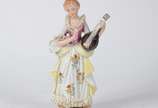 Estatueta de porcelana policromada representand... - Estatueta de porcelana policromada representando jovem com instrumento de cordas.