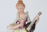Estatueta de porcelana policromada representand... - Estatueta de porcelana policromada representando jovem com instrumento de cordas.
