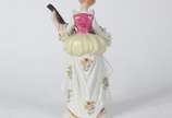Estatueta de porcelana policromada representand... - Estatueta de porcelana policromada representando jovem com instrumento de cordas.