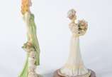 Duas estatuetas de resina policromada represent... - Duas estatuetas de resina policromada representando figuras femininas com flores e frutos.