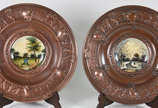 Par de medalhões em cobre ricamente cinzelados,... - Par de medalhões em cobre ricamente cinzelados, parte central de porcelana com paisagens em policromia.