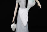Escultura de porcelana ao gosto Lladro represen... - Escultura de porcelana ao gosto Lladro representando figura feminina com jarros. Altura 35 cm.
