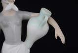 Escultura de porcelana ao gosto Lladro represen... - Escultura de porcelana ao gosto Lladro representando figura feminina com jarros. Altura 35 cm.