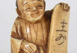 Netsuke de marfim representando figura com placa. - Netsuke de marfim representando figura com placa.