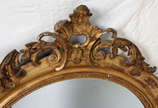 Espelho de cristal feitio oval com moldura de m... - Espelho de cristal feitio oval com moldura de madeira dourada encimada por guirlanda entalhada (pequenos defeitos).