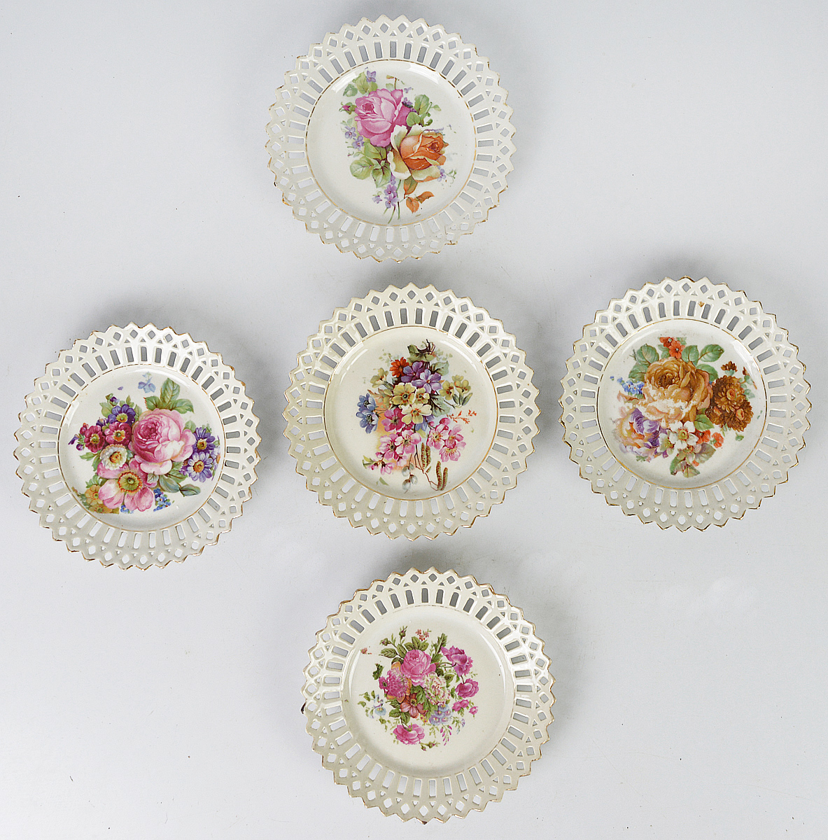 Conjunto composto por cinco pratos em porcelana com bordas vazadas...