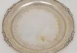 Salva circular em prata brasileira cinzelada. B... - Salva circular em prata brasileira cinzelada. Borda ornamentada por composições estilizadas em relevo, centralizando arranjos com volutas e flor...