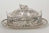 Manteigueira em prata de formato oval com tampa... - Manteigueira em prata de formato oval com tampa e presentoir. Bojo lavrado e vazado com varetas sustentando adornos recortados com animais e árv...