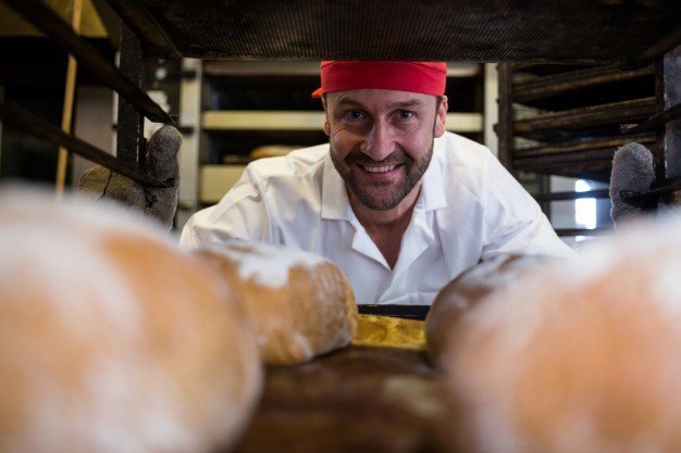 Sorrindo padeiro mantendo a bandeja de paes assados na prateleira 1170 2183