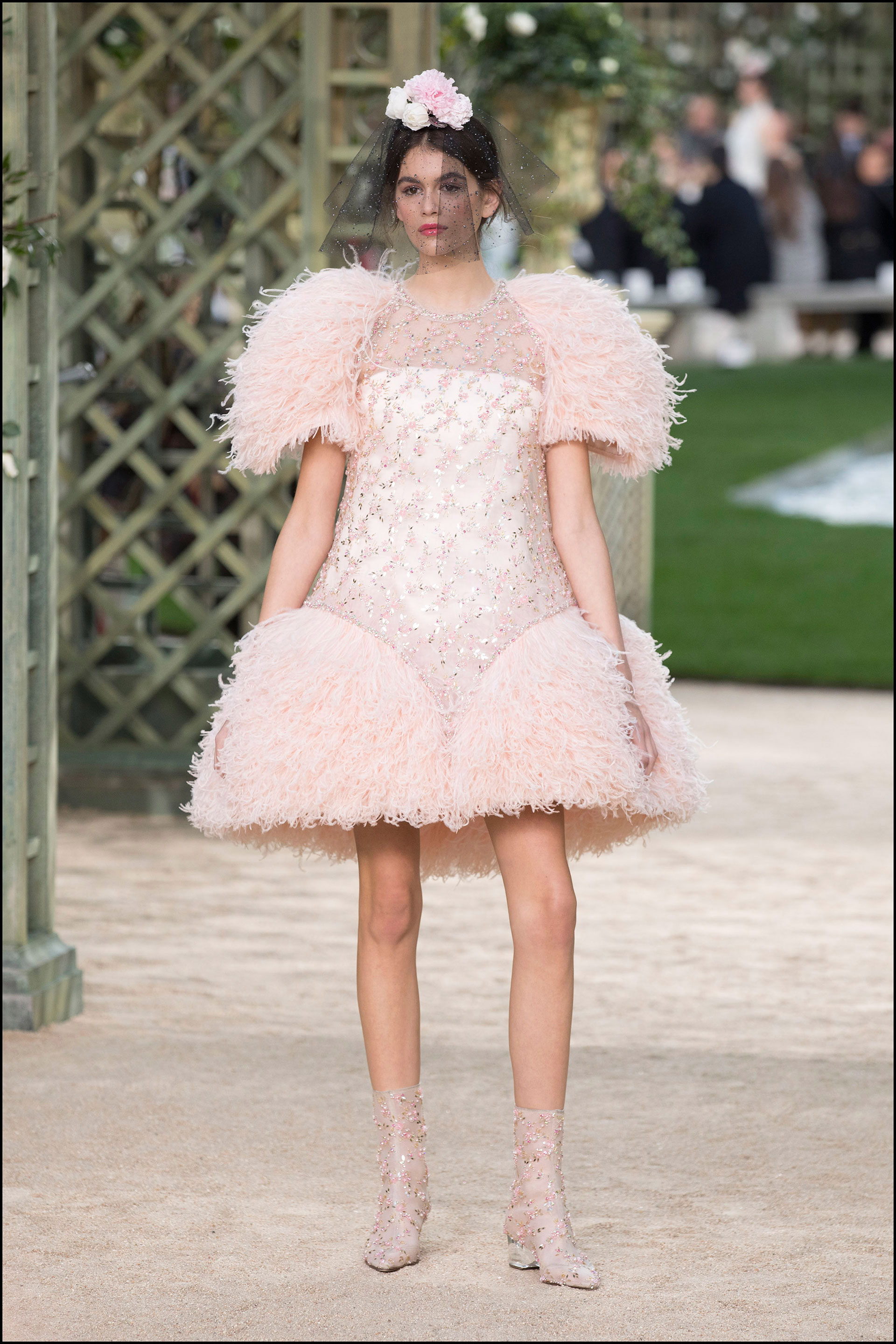 Kaia Gerber con un diseño corto bordado con plumas, botas, y flores en el pelo.