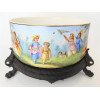 <p>Sèvres - Centro de mesa circular, de porcelana europeia, decorado com cenas domésticas familiares, sobre base de madeira, com 3 pés de bicho - Com marca no fundo - 25 cm diâm</p>