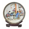 <p>Elegante prato decorativo oriental em porcelana esmaltada e policromada, decorado com cena cortesã oriental composta por personagens em interior palaciano, ricamente detalhada e ideogramas, com borda em reservas ornamentais, com 27 cm diâm, com selo azul no fundo, sobre apoio de madeira.</p>