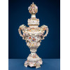 <p>Grande &acirc;nfora ornamental de porcelana policromada alem&atilde;, marca Sitzendorfer 1884 a 1902, ricamente decorada com abundantes aplica&ccedil;&otilde;es florais em relevo, apresentando bojo com pintura floral, al&ccedil;as vazadas de movimento rocaille e tampa encimada por bouquet floral. Base e corpo ornamentados com relevos, doura&ccedil;&atilde;o e flores aplicadas. No fundo, marca azul emulando as famosas espadas cruzadas de Meissen - 85 cm alt - Europa, s&eacute;c XIX/XX</p>