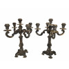 <p>Par de candelabros de cinco luzes em metal prateado, ricamente ornamentados em estilo clássico, com braços curvos, fustes decorados em relevo e bases quadripés com elementos vegetalistas - 37 cm de altura.</p>