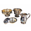 <p>Lote com 4 peças avulsas de metal prateado, composto por 1 centro de mesa com pegas de cabeça de leão (17 cm alt), 1 jarra (22 cm alt) com pequena mossa na base, 1 balde de gelo (22 cm alt) e 1 pote com tampa (7 cm alt). Bordas decoradas em relevo</p>