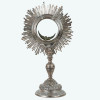 <p>Magnífico e raro ostensório/custódia neoclássica em prata cinzelada, repuxada e burilada. Hostiário circular com resplendor raiado decorado com elementos alusivos à eucaristia, porta móvel em vidro biselado com moldura e ao centro lúnula em forma de cabeça de anjo alada. Fuste assente sobre base circular gomada, em forma de campânula e decorados com motivos vegetalistas. Brasil, séc. XIX. Peso bruto: 1.220 gramas. Dimensões: 40 x 22 x 15 cm.</p>