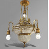 LUSTRE EMPIRE — FRANÇA, ESTILO NAPOLEÃO III, SÉCULO XIX<br />Bronze cinzelado e dourado | Contas de cristal | Iluminação central e pendente<br />Pinhas, palmetas, ânforas, guirlandas, laçarotes e franjas<br />Medidas: 80 x 50 x 50 cm<br /><br />Magnífico lustre estilo Império, França, Segundo Império/Napoleão III, c. 1860–1880, em bronze cinzelado e dourado com contas de cristal lapidado. Corpo central em forma de cesto, totalmente revestido de cristais. Três braços pendentes na orla, com arandelas em forma de ânforas para velas ou lâmpadas. Iluminação central com bacia de luz e bojo inferior também em cristal. Rica ornamentação neoclássica: pinhas, palmetas, florões, guirlandas de louro, laçarotes, cortinados, franjas e caneluras — todo o repertório Império/Napoleão III. Remate superior com coroa de bronze e corrente de suspensão.<br /><br />Estilo: Napoleão III, 1852–1870<br />O Segundo Império foi o auge do ecletismo francês. O estilo Napoleão III retoma o Império de Bonaparte, 1804–1815, mas com mais opulência: mistura Neoclássico, Luís XVI e Barroco. É o estilo dos palácios, óperas e hotéis de luxo de Paris. Este lustre tem o vocabulário completo: ânforas = antiguidade, palmetas = Egito, guirlandas e laçarotes = Luís XVI, franjas = teatralidade.<br /><br />Modelo “corbeille”, cesto, era o mais luxuoso do Segundo Império. O bojo inferior em cristal difunde a luz. Os três braços pendentes eram para velas de cera — a iluminação elétrica foi adaptada depois, mantendo os soquetes em forma de ânfora. Peça para salão nobre, hall ou sala de jantar de palacete.<br /><br />Técnica: Bronze douré + Cristal<br />Bronze cinzelado à mão e dourado a mercúrio. As contas de cristal lapidadas em facetas octogonais para máximo brilho. Fundição impecável, típica de Paris, c. 1870.