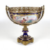 <p>Grande centro de mesa em porcelana esmaltada em azul-cobalto, com rica decora&ccedil;&atilde;o representando cena de casal. Pe&ccedil;a com corpo em bronze dourado, com trabalho em alto-relevo e marca da manufatura francesa. 52 cm de alt.; 51 x 30 cm. Fran&ccedil;a, s&eacute;c. XIX. (Pe&ccedil;a com restauro)</p>