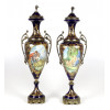 <p>Belo par de ânforas em porcelana esmaltada na tonalidade azul-cobalto, com rico trabalho em esmalte, representando cena de casal, adornadas em dourado, com pé e alças laterais em bronze dourado. França, séc. XIX. 62 cm de alt.</p> <p>Belo par de ânforas em porcelana esmaltada na tonalidade azul-cobalto, com rico trabalho em esmalte, representando cena de casal, adornadas em dourado, com pé e alças laterais em bronze dourado. França, séc. XIX. 62 cm de alt.</p>
