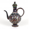 <p>Belíssimo bule japonês em cloisonné (esmaltado com separações metálicas), de corpo globular sobre base anelada, bico fino curvado e alça arqueada, acompanhado de tampa original com botão em formato de flor. A peça é inteiramente decorada com ricas reservas ornamentais, destacando, de um lado, uma fênix (hou-ou) em voo, com plumagem policromada em tons de verde, azul, amarelo e vermelho, e, do outro, borboletas entre flores estilizadas sobre fundo acobreado. O pescoço da peça é decorado com padrões florais multicoloridos sobre fundo azul-escuro, emoldurado por frisos geométricos e motivos florais tradicionais. A técnica do cloisonné, com fios de cobre formando as células preenchidas por esmaltes vítreos, demonstra o refinamento e a precisão da produção japonesa voltada ao mercado de exportação durante o período Meiji. Japão. 18 cm de alt.</p> <p>Belíssimo bule japonês em cloisonné (esmaltado com separações metálicas), de corpo globular sobre base anelada, bico fino curvado e alça arqueada, acompanhado de tampa original com botão em formato de flor. A peça é inteiramente decorada com ricas reservas ornamentais, destacando, de um lado, uma fênix (hou-ou) em voo, com plumagem policromada em tons de verde, azul, amarelo e vermelho, e, do outro, borboletas entre flores estilizadas sobre fundo acobreado. O pescoço da peça é decorado com padrões florais multicoloridos sobre fundo azul-escuro, emoldurado por frisos geométricos e motivos florais tradicionais. A técnica do cloisonné, com fios de cobre formando as células preenchidas por esmaltes vítreos, demonstra o refinamento e a precisão da produção japonesa voltada ao mercado de exportação durante o período Meiji. Japão. 18 cm de alt.</p>