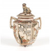 <p>Elegante incensário hexagonal em porcelana Satsuma, com tampa perfurada e botão em forma de shishi (cachorro-leão guardião), finamente modelado e esmaltado. O corpo apresenta delicadas reservas emolduradas, decoradas com cenas de paisagens florais, incluindo ramos de cerejeiras em flor, bambus e crisântemos, minuciosamente delineados em esmaltes policromados e ricos detalhes em ouro. As duas alças laterais, de formato angular, harmonizam com a forma facetada do corpo, que repousa sobre três pequenos pés. A tampa, emoldurada por frisos geométricos e florais, possui perfurações para a liberação da fumaça do incenso. A base exibe a típica marca vermelha com o brasão Shimazu e a inscrição Touya Hitsuyaki - Tomonobu, indicando produção artesanal da escola Satsuma no período Meiji (1868–1912). 23,5 cm de alt. (com tampa e shishi); 14 cm de alt. (sem tampa). (Necessita de restauro na tampa).</p> <p>Elegante incensário hexagonal em porcelana Satsuma, com tampa perfurada e botão em forma de shishi (cachorro-leão guardião), finamente modelado e esmaltado. O corpo apresenta delicadas reservas emolduradas, decoradas com cenas de paisagens florais, incluindo ramos de cerejeiras em flor, bambus e crisântemos, minuciosamente delineados em esmaltes policromados e ricos detalhes em ouro. As duas alças laterais, de formato angular, harmonizam com a forma facetada do corpo, que repousa sobre três pequenos pés. A tampa, emoldurada por frisos geométricos e florais, possui perfurações para a liberação da fumaça do incenso. A base exibe a típica marca vermelha com o brasão Shimazu e a inscrição Touya Hitsuyaki - Tomonobu, indicando produção artesanal da escola Satsuma no período Meiji (1868–1912). 23,5 cm de alt. (com tampa e shishi); 14 cm de alt. (sem tampa). (Necessita de restauro na tampa).</p>