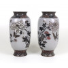 <p>Magnífico par de vasos japoneses de cloisonné, de corpo ovóide alongado e base circular, com fundo em esmalte branco opaco. A decoração minuciosa, em esmalte preto e cobre dourado, apresenta ramos floridos de crisântemos e peônias entremeados por borboletas em pleno voo, compondo uma cena de grande delicadeza e elegância. As bordas superiores e inferiores são ricamente ornamentadas com frisos florais em esmalte azul, verde e vermelho. O interior é esmaltado em tom azul esverdeado. Peças de alta qualidade, datáveis do período Taisho (c. 1910-1925), destinadas à exportação de luxo -Japão 33 cm alt. 14 cm diâm.</p>